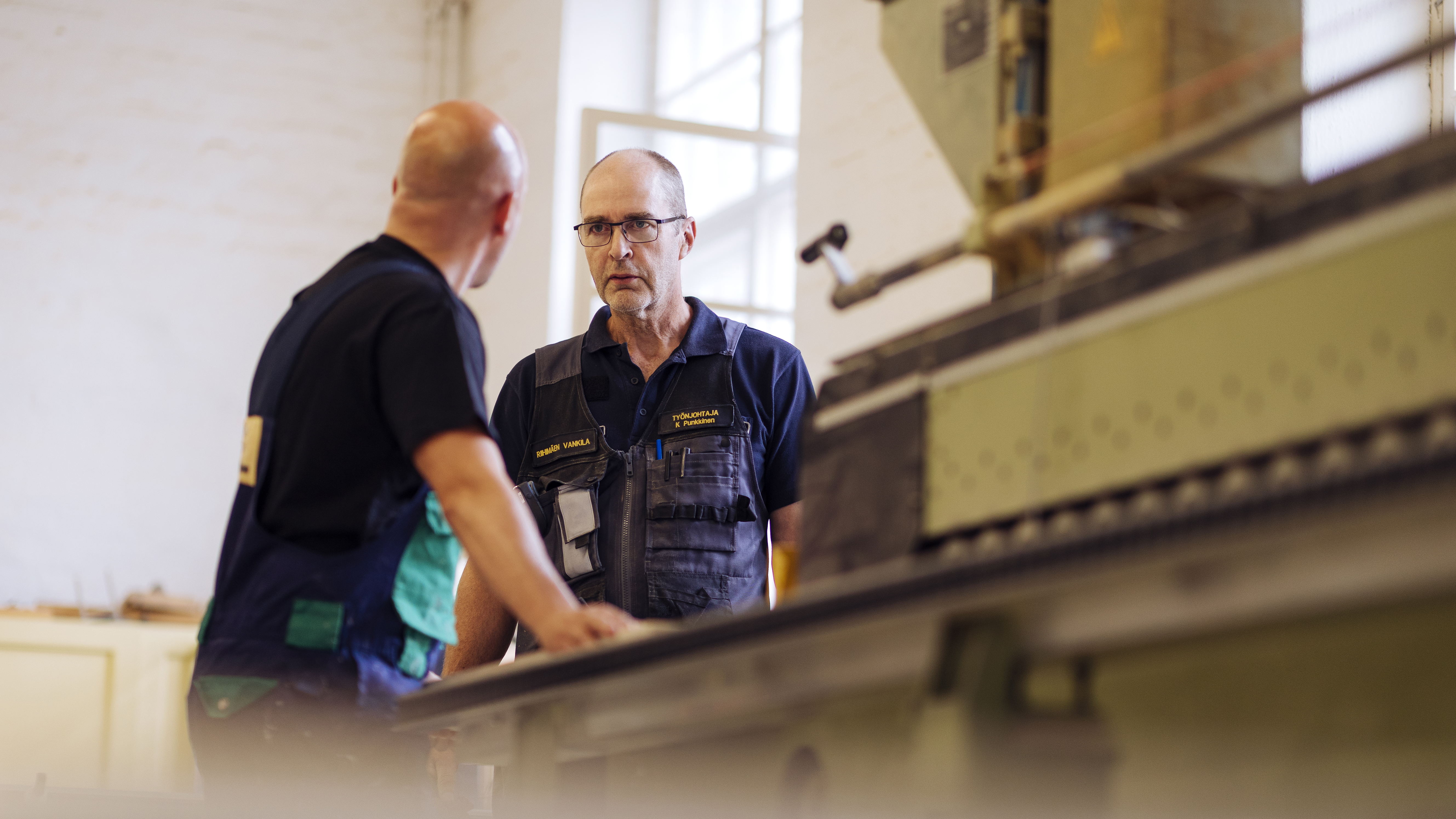 A work supervisor and a prisoner stand next to a machine.