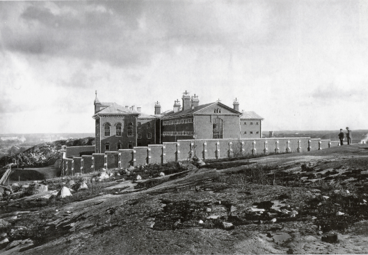 Vanha mustavalkokuva suuresta, korkean aitauksen keskellä olevasta vankilasta.