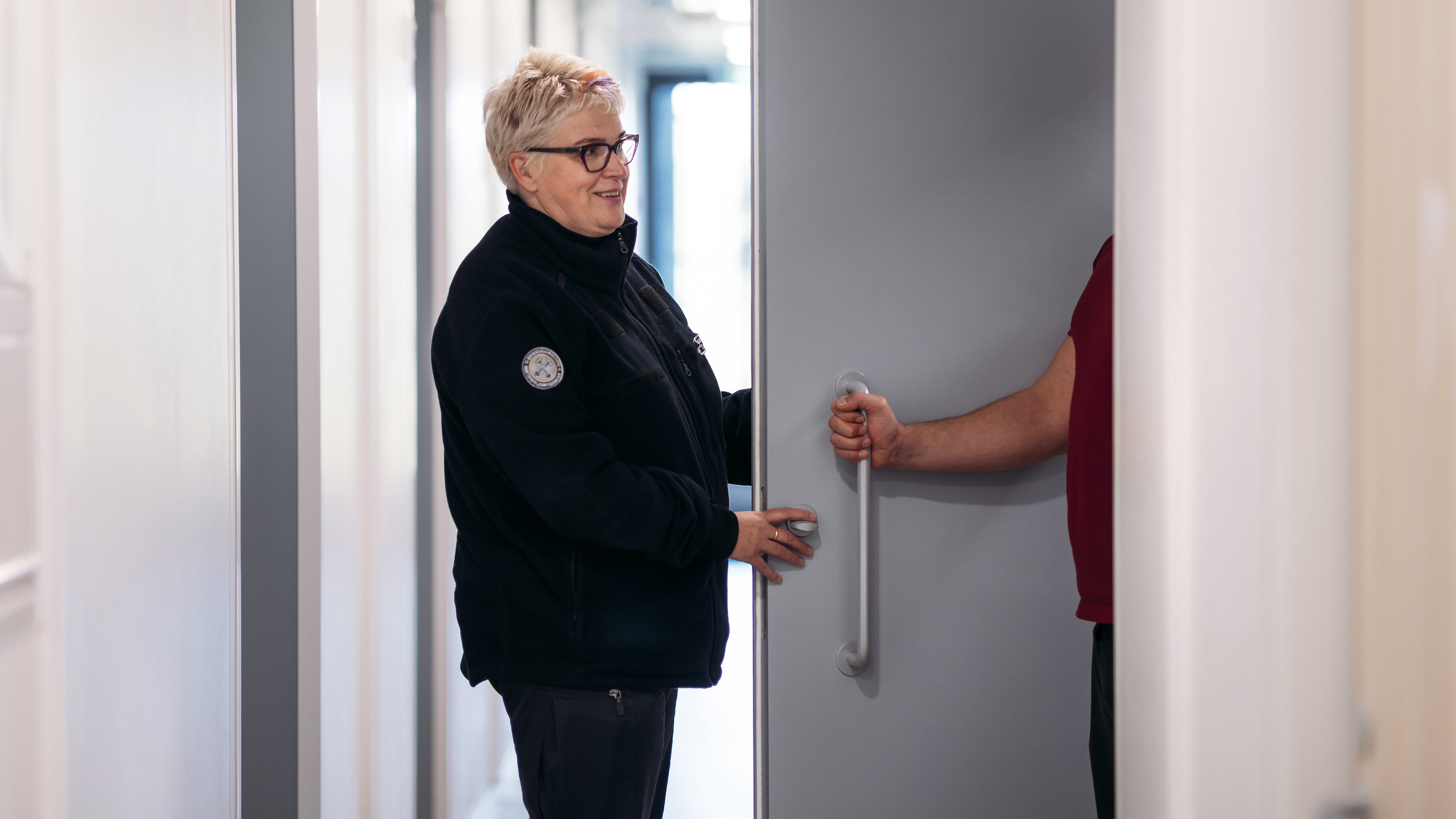An official of the Prison and Probation Service stands outside a cell and holds the door. A hand of a person, who is inside the cell, holds the door handle.